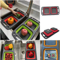 Collapsible over-sink dual colander and strainer set in use, showing foldable silicone baskets with fruits and vegetables
